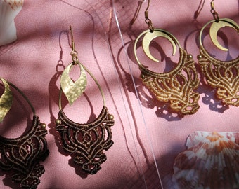 May include: Close-up of handmade earrings. The earrings feature a brass leaf and a macrame design in shades of brown and gold. One pair has a crescent moon design. The earrings are displayed on a pink surface.