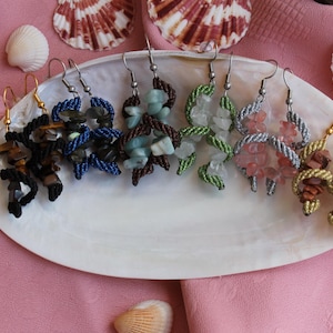 May include: A set of six pairs of earrings featuring different colored stones and beaded designs. The earrings are displayed on a white, seashell-shaped plate.