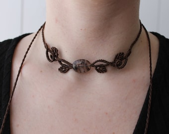 May include: A brown cord choker necklace with a dark gray oval gemstone pendant and a knotted leaf design.