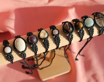 May include: A set of nine black macrame bracelets with different colored gemstone beads. The bracelets are displayed on a wooden stand.