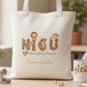 May include: A white canvas tote bag with the word "NICU" in a giraffe print font, featuring animal illustrations. The text "Protector of tiny humans" and a name are printed below. A matching mug is also visible.