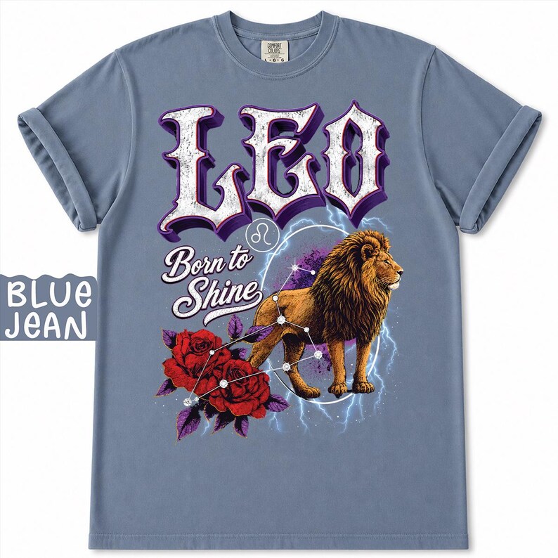 Op de afbeelding: Een blauw spijkerkleurig t-shirt met een afbeelding van een leeuw, rode rozen en de tekst LEO en Born to Shine. Het ontwerp bevat een sterrenbeeldpatroon, een cirkelvormige omtrek en blauwe bliksemeffecten op de voorzijde.