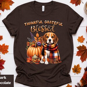 Peut inclure: Un t-shirt à manches courtes marron chocolat foncé avec un motif représentant un chien beagle portant une écharpe à carreaux, assis à côté d'une citrouille et d'une tasse de café. Le texte au-dessus du chien indique THANKFUL GRATEFUL BLESSED.
