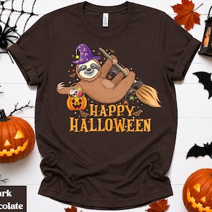 May include: A dark chocolate brown t-shirt featuring a graphic of a sloth wearing a purple witch hat, riding a broomstick, and holding a jack-o'-lantern candy bucket. The text "HAPPY HALLOWEEN" is printed in yellow below the sloth illustration.