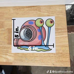May include: A sticker featuring a cartoon snail with a turbocharger shell. The snail is pink with blue spots and green eyes. The sticker measures 5 inches tall and 6 inches wide, with the text "Precision Turbo".