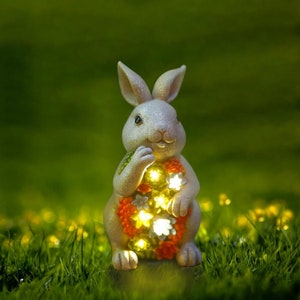 May include: A white ceramic rabbit figurine with a floral design and built-in LED lights. The rabbit is holding a bouquet of flowers in its paws.