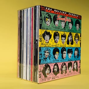 May include: A collection of vinyl records in a clear plastic storage case. The front of the case features a colorful advertisement for The Rolling Stones album "Some Girls". The ad features a grid of images of the band members and the album title.