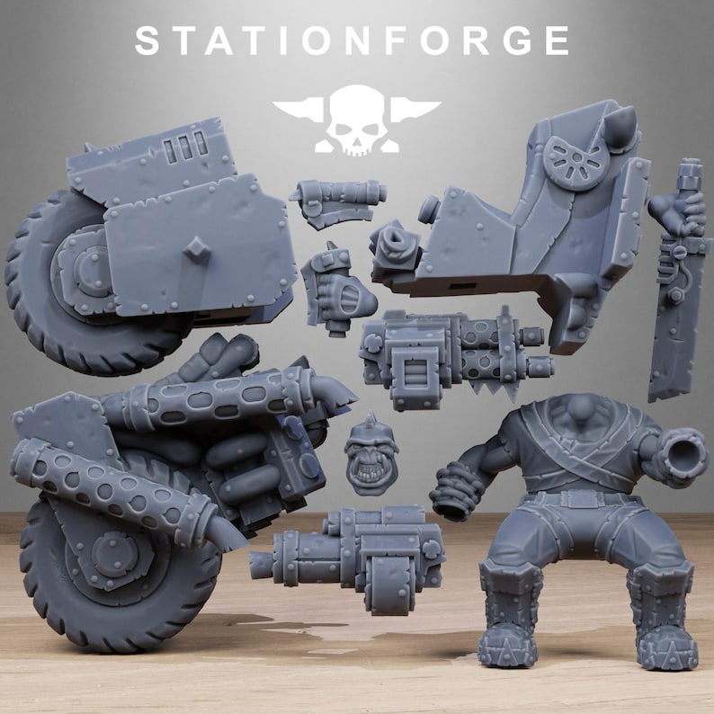 May include: Gray plastic model kit of a futuristic vehicle and a figure, with the text "STATIONFORGE" and a skull logo. The kit includes various components like wheels, weapons, and body parts, suggesting a miniature war game theme.
