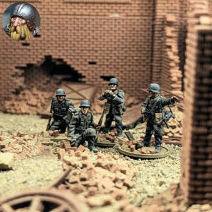 以下が含まれることがあります： グレーの制服とヘルメットを着用した兵士のミニチュアフィギュア。レンガ造りの廃墟がある、戦争で荒廃した環境に配置されています。1体のフィギュアがひざまずき、他のフィギュアはライフルや装備を持って立っています。砂地の土台に瓦礫が散らばっています。