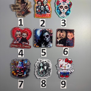 Può includere: Una collezione di nove spille in acrilico a tema Halloween. Le spille presentano vari personaggi e disegni di film horror, tra cui Freddy Krueger, la maschera di Scream, un teschio di zucchero, Chucky e Hello Kitty. Ogni spilla ha un bordo glitterato.