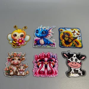 May include: A collection of six glittery, cartoon-style stickers. The stickers feature a bee, a blue dragon, sunflowers with butterflies, a cow and calf, two flamingos, and a black and white cow. Each sticker has a glittery border.