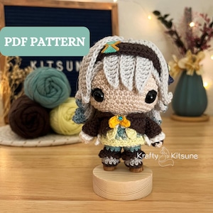 Puede incluir: Muñeca amigurumi de crochet con cabello gris, ojos marrones y un atuendo marrón y amarillo. La muñeca está de pie sobre una base de madera. La imagen incluye el texto "Krafty Kitsune".