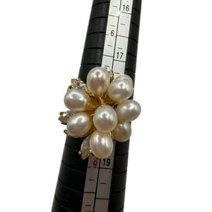 May include: A gold-toned ring featuring a cluster of white oval pearls and small clear marquise-cut stones. The ring is positioned on a black ring mandrel, with the band size clearly indicating a measurement between 8 and 9 on the scale.