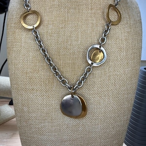 May include: Silver-tone chain necklace with gold and silver-tone pendant and circular accents. The necklace features a large, layered pendant and several gold-toned circular and teardrop-shaped accents.