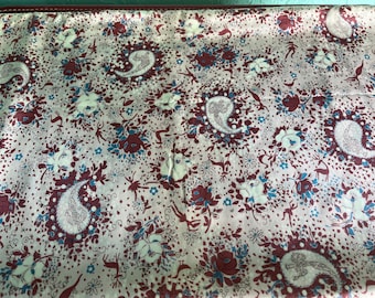 May include: A white fabric with a paisley pattern in shades of burgundy and blue. The fabric is covered in a repeating pattern of paisley shapes, flowers, and small birds.
