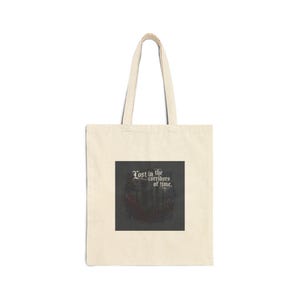 May include: A cream-coloured tote bag with a rectangular graphic. The graphic displays the text "Lost in the corridors of time" in a gothic font, above a dark, blurred image. The bag has two handles for carrying.