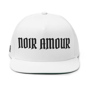 Puede incluir: Gorra blanca de ala plana con las palabras "NOIR AMOUR" en letras góticas negras en la parte delantera. La gorra tiene la parte inferior de la visera verde y un pequeño logotipo en el lateral.