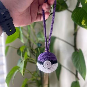 May include: Purple and white crocheted Poké Ball keychain with a black ring around the center.