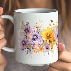 Puede incluir: Taza de cerámica blanca con un diseño de acuarela de flores moradas, amarillas y rosas con una abeja en el lateral.