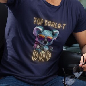 May include: A navy blue t-shirt with a graphic of a koala wearing sunglasses and a bow tie. The text "Top Koala-T Dad" is printed in yellow on the shirt.