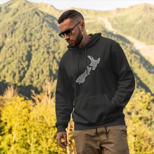 May include: A black hoodie with a white outline of the islands of New Zealand.