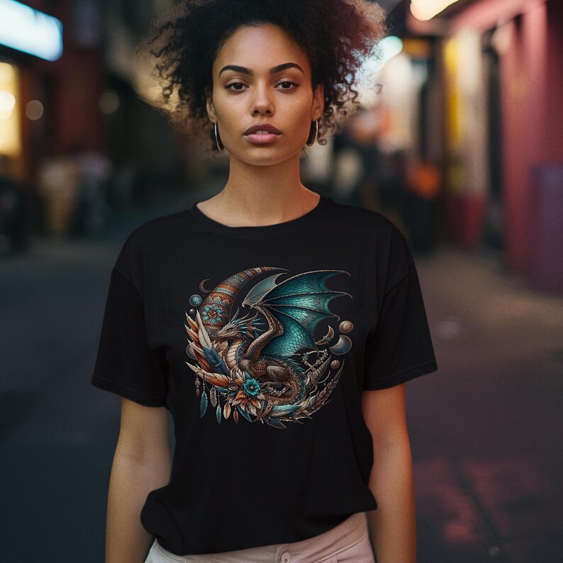 This image features a woman in a black t-shirt that has a vivid brown & turquoise dragon with dark boho style moon, feathers and accessories. It also has color choices and printing info on the image.