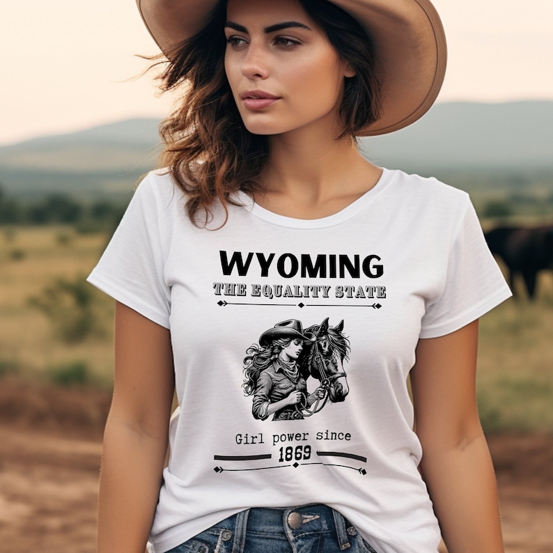 This short sleeve T-Shirt features a black and white line drawing style, cowgirl and her horse with the words: Wyoming, the equality State.  Girl Power since 1869. The large design is centered on the front of the T-Shirt.