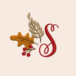 May include: Embroidered design featuring a red letter "S" with autumn leaves and berries. The design includes a golden-yellow leaf, a beige leaf, and small red berries, all on a cream-colored background. This design is suitable for fall-themed crafts.