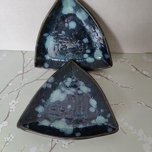 May include: Two triangular ceramic dishes with a dark blue glaze and white speckles. The dishes are stacked on top of each other.