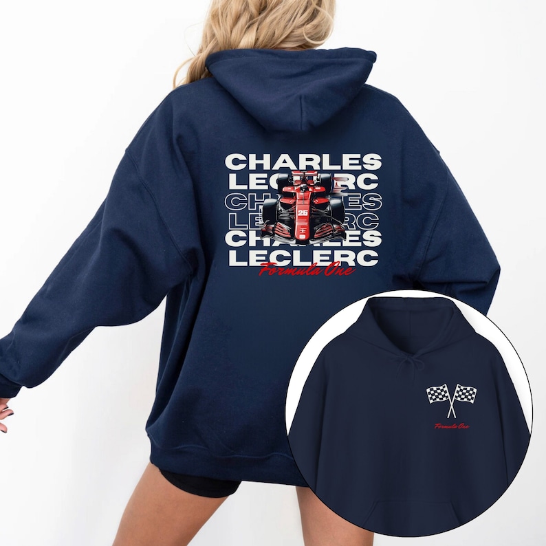 May include: Navy blue hoodie with a white graphic on the back featuring the text "CHARLES LECLERC" repeated in a staggered pattern with a red Formula One race car in the center. The text "Formula One" is below the car. The front of the hoodie has a small white graphic of two checkered flags with the text "Formula One" below.