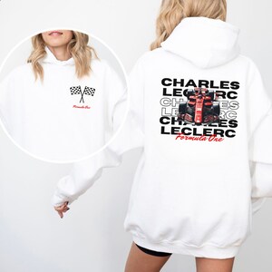 May include: White hoodie with a checkered flag graphic on the front and a graphic of a race car and the text "CHARLES LECLERC Formula One" on the back.