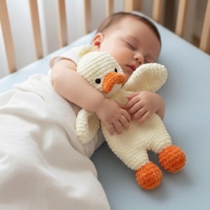 May include: A cream-colored crochet duck plush toy with a bright orange beak and feet. The stuffed animal features a soft, textured yarn construction with small black eyes, designed as a simple, flat-bodied companion for comfort and play.