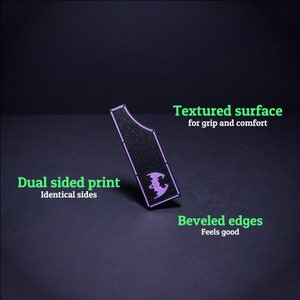 May include: Black, textured grip with a purple bat design. Features dual-sided printing and beveled edges. The text on the image says "Textured surface for grip and comfort", "Dual sided print Identical sides", and "Beveled edges Feels good".