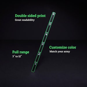 Op de afbeelding: Een zwarte meetlat met een groene rand en witte cijfers van &eacute;&eacute;n tot zes. De tekst op de afbeelding luidt: Double sided print, Great readability, Full range 3" to 12", Customize color, Match your army. De lat staat in een diagonale hoek.