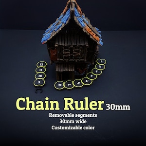 Könnte beinhalten: Ein Miniatur-Holzhaus mit blauem und orangefarbenem Dach wird neben einem Kettenlineal gezeigt. Das Lineal besteht aus schwarzen, nummerierten Segmenten mit gelben Umrissen. Der Text "Chain Ruler 30mm" ist sichtbar.