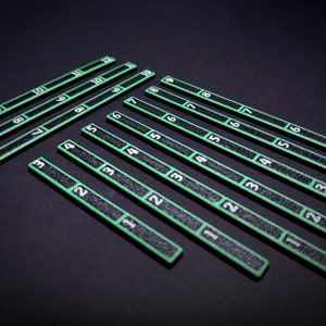 Op de afbeelding: Een verzameling lange, dunne, rechthoekige markers met een getextureerd zwart oppervlak en felgroene randen. Elke marker is verdeeld in segmenten, met witte cijfers in elke sectie, vari&euml;rend in volgorde van &eacute;&eacute;n tot twaalf.