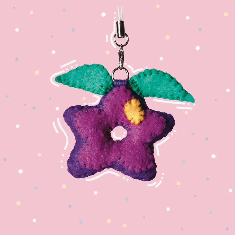Pu&ograve; includere: Portachiavi a forma di stella in feltro viola con un centro in feltro giallo e foglie in feltro verde. Il portachiavi &egrave; attaccato a una catena argentata.
