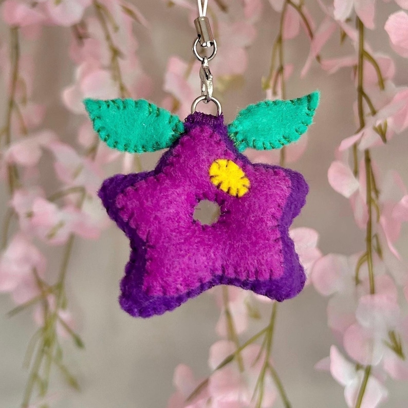 Pu&ograve; includere: Portachiavi a forma di stella in feltro viola con un centro giallo e foglie in feltro verde.
