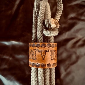 May include: A brown leather rope with a decorative leather cuff. The cuff has the initials "MTD" and a bull skull design.