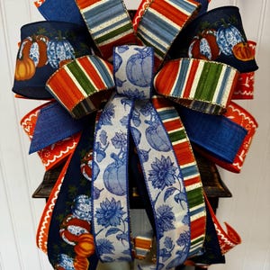May include: A decorative bow featuring various ribbons in navy, orange, and blue. Some ribbons display pumpkin and floral patterns, while others have striped designs. The bow is likely for seasonal or holiday decor.