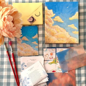 以下が含まれることがあります： 青い空と雲の小さな絵、封筒、筆など、さまざまな画材と文房具。 青、黄、桃色の色使いで、チェック柄の背景です。