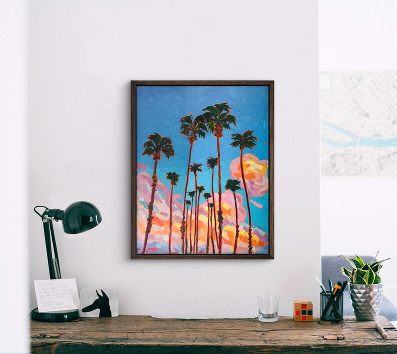 May include: An oil painting of palm trees against a blue sky with pink and orange clouds. The artwork is framed in a dark brown wooden frame. The painting depicts tall, slender palm trees with green fronds.