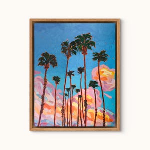 May include: An oil painting of palm trees against a blue sky with pink and orange clouds. The artwork is framed in a natural wood frame. The palm trees are tall and slender, with green fronds at the top.