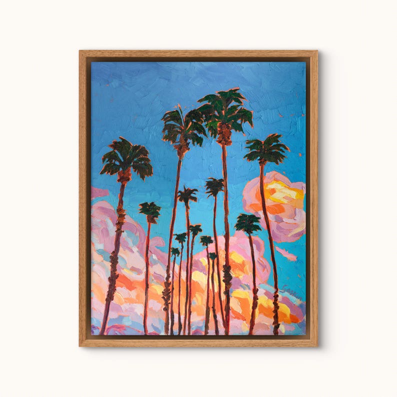 May include: An oil painting of palm trees against a blue sky with pink and orange clouds. The artwork is framed in a natural wood frame. The palm trees are tall and slender, with green fronds at the top.