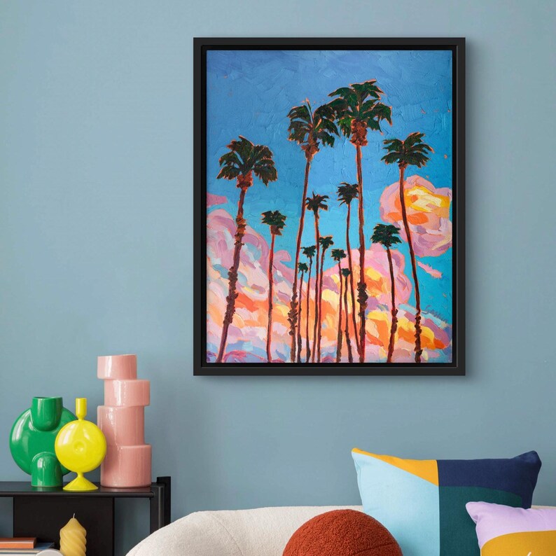 May include: An oil painting of palm trees against a blue sky with pink and orange clouds. The artwork is framed in a black rectangular frame. The painting has a vibrant, colorful aesthetic.