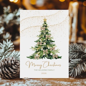 May include: A Christmas card featuring a watercolour illustration of a decorated Christmas tree. The card has the text "Merry Christmas" in gold script, a family name, and the year 2026. Gold glitter accents the top of the card.