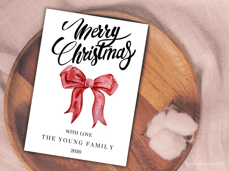 May include: A white Christmas card with the words "Merry Christmas" in elegant black script. A watercolor-style red bow is centered below the text. The card includes the text "With Love, The Young Family, 2030".