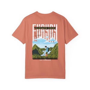 May include: Terracotta-colored t-shirt featuring a graphic of a person hiking in a mountain landscape. The text "ELEVATE YOUR" is printed in white above the illustration. The brand name "CUT THREADS" is printed at the bottom.