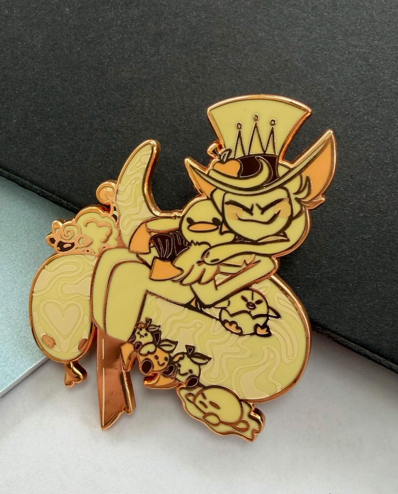 May include: A yellow enamel pin featuring a cartoon character with a top hat and a duck. The pin has a gold outline and is surrounded by other cartoon characters. The pin is on a dark surface.