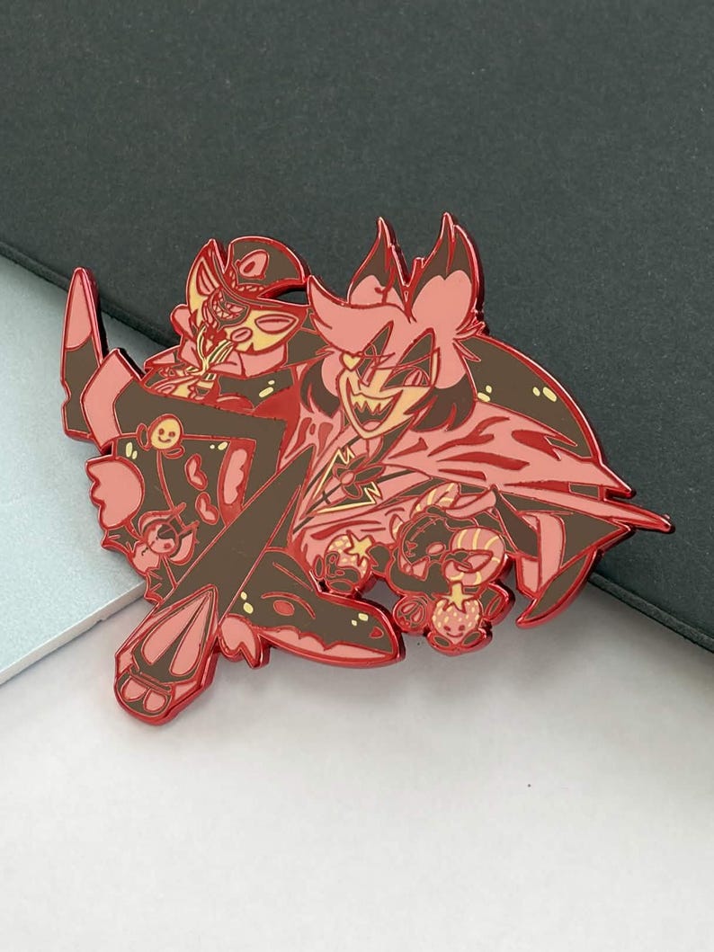 May include: A red and brown enamel pin featuring two cartoon characters with sharp teeth and expressive faces. The pin has a detailed design with a glossy finish, perfect for collectors or fans of animation.